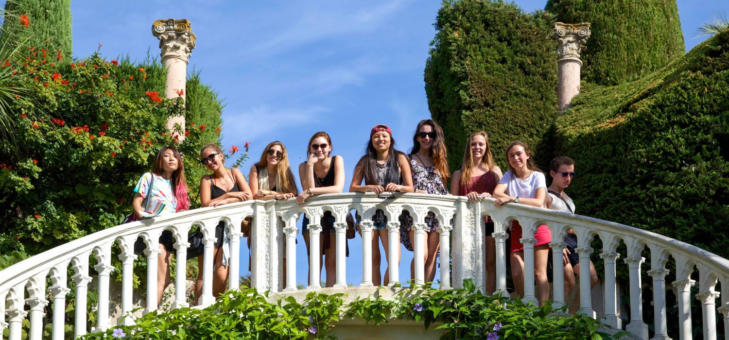 Semester students on a bridge in Nice, surrounded by greenery with blue sky and ancient columns behind.